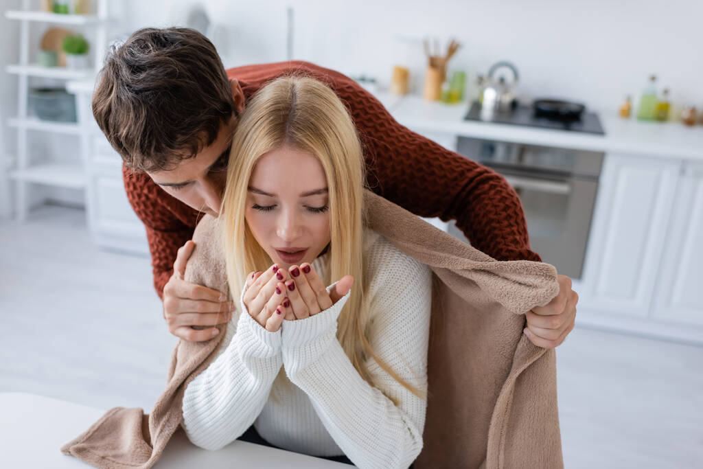 caring boyfriend in sweater holding blanket near freezing blonde girlfriend  - Photo, Image
