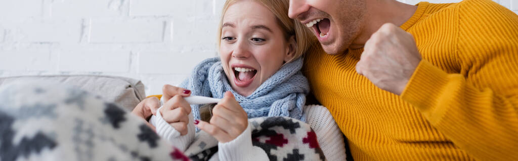 excited man and sick blonde woman looking at digital thermometer, banner - Photo, Image