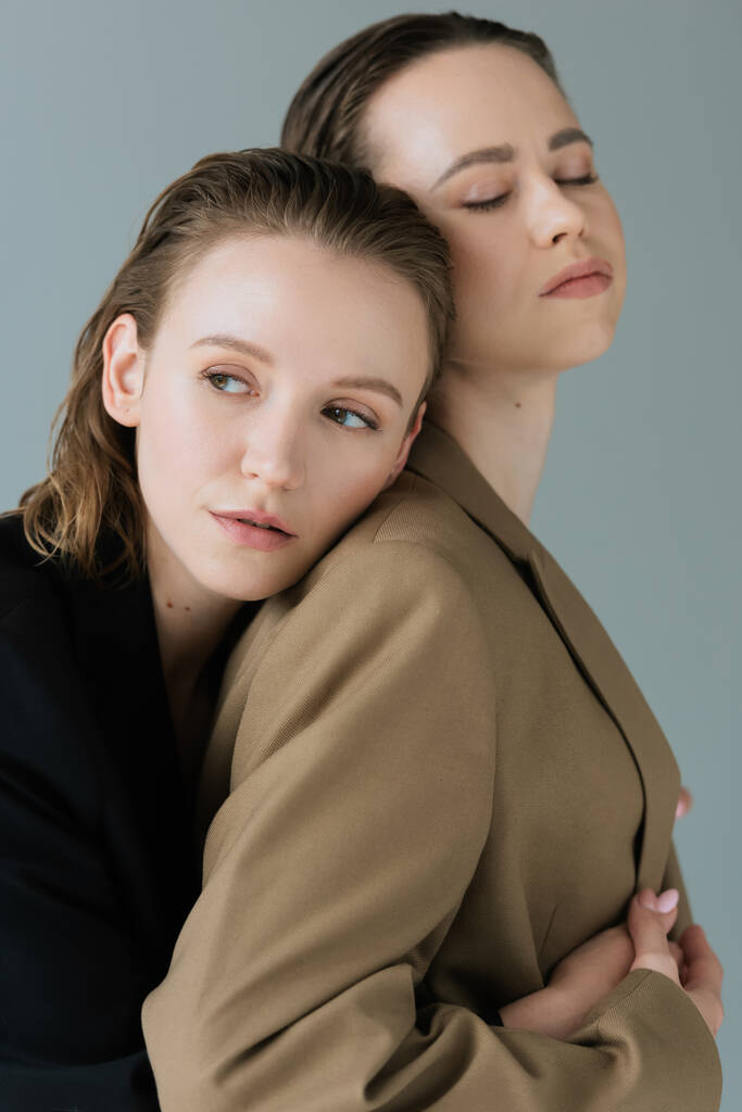 smyslné lesbičky žena opírající se o mladé přítelkyně stojící se zavřenýma očima izolované na šedé - Fotografie, Obrázek