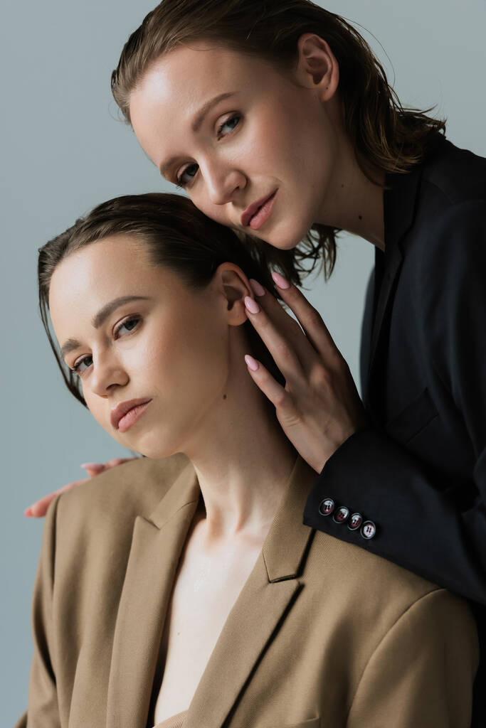 young and sensual lesbian couple in blazers looking at camera isolated on grey - Photo, Image