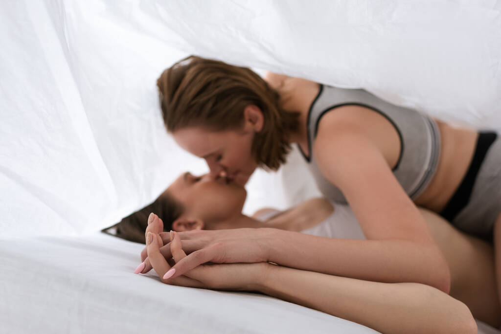 hämärtynyt lesbot kädestä ja suudella kun makaa valkoisen peiton alla - Valokuva, kuva