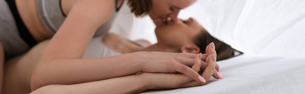 Şehvetli lezbiyen aşıkların el ele tutuşup arka planda beyaz battaniyenin altında öpüşmelerinin yan görüntüsü. - Fotoğraf, Görsel