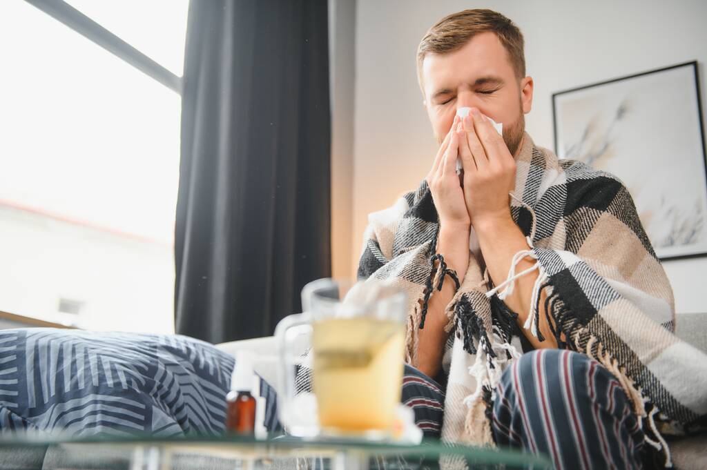 Хвора людина сидить вдома на сірому дивані з ковдрою. Хвороба, захист, коронавірус, хвороба, грип
. - Фото, зображення