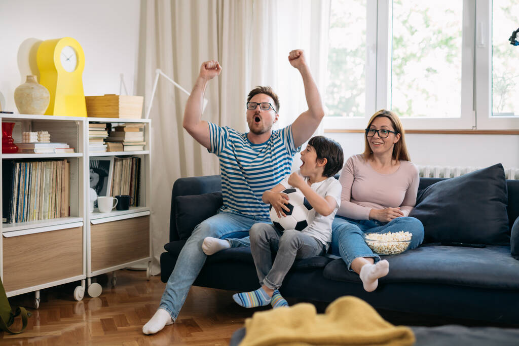 rodzina trojga oglądających mecz piłki nożnej w ich domu - Zdjęcie, obraz
