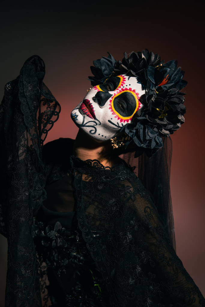 Frau im schwarzen Kostüm und Cartina-Make-up blickt in die Kamera auf weinrotem Hintergrund  - Foto, Bild