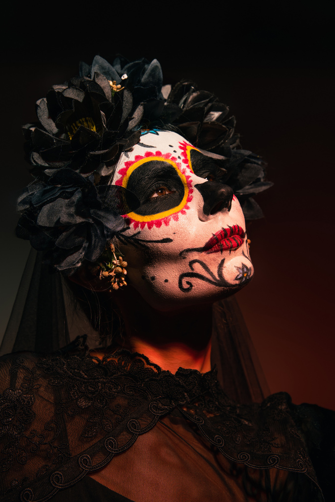 Портрет женщины в мексиканский день мертвого костюма, стоящей на бордовом фоне  - Фото, изображение
