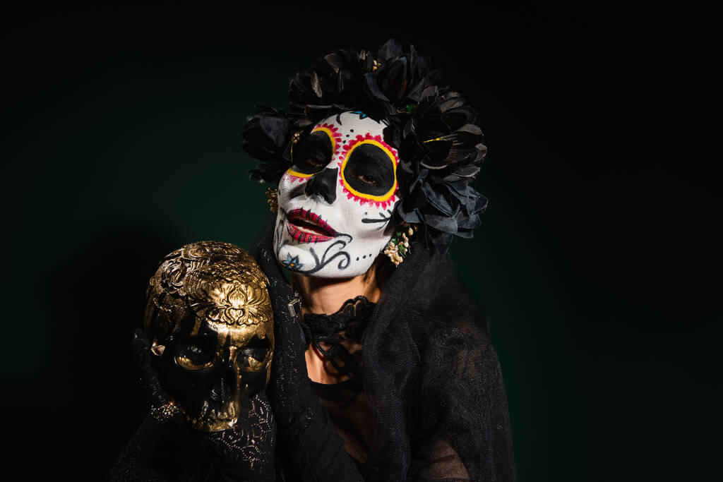 Žena v mexickém kostýmu Santa Muerte drží lebku na tmavozeleném pozadí  - Fotografie, Obrázek