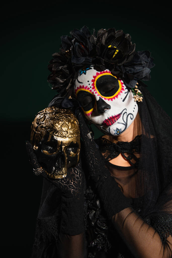 Retrato de mujer en día de disfraz muerto sosteniendo cráneo sobre fondo verde oscuro  - Foto, imagen