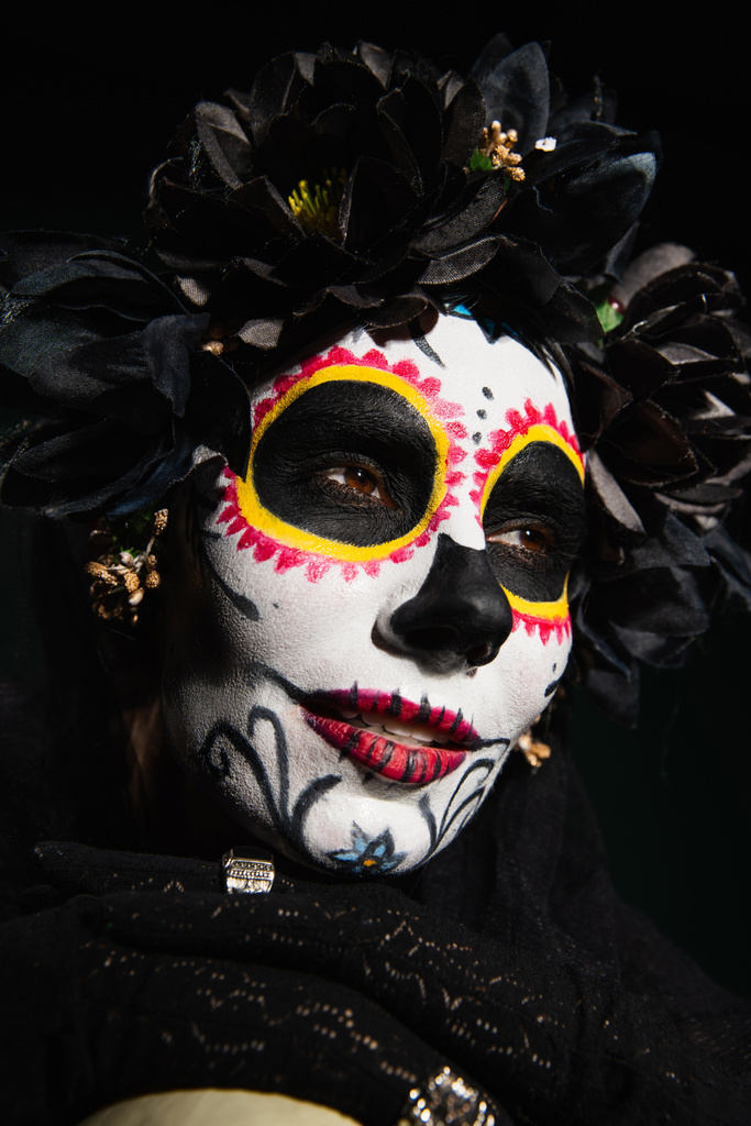 Portrait of woman in mexican santa muerte costume looking away isolated on black  - Photo, Image