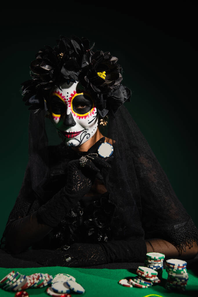 Kobieta w Santa Muerte kostium halloween gospodarstwa Chip gry na ciemnozielonym tle  - Zdjęcie, obraz