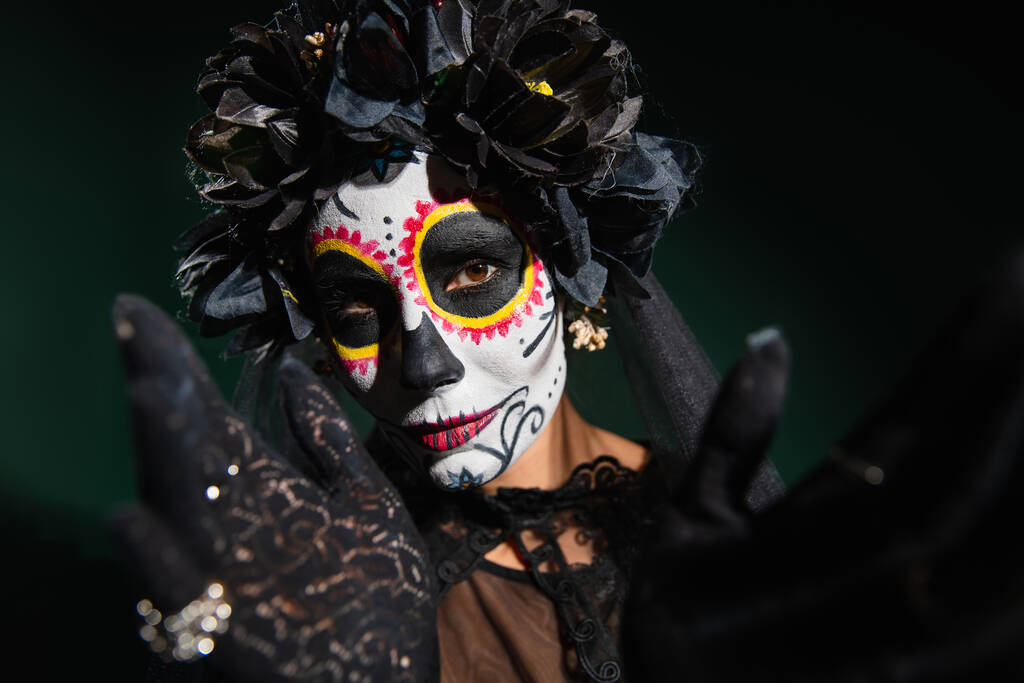 Женщина в сахарном черепе макияж и гаечный ключ с черными цветами, глядя на камеру на темно-зеленом фоне  - Фото, изображение