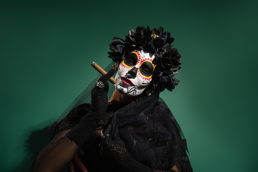 Mujer en disfraz de Halloween espeluznante y maquillaje celebración cigarro sobre fondo verde  - Foto, imagen