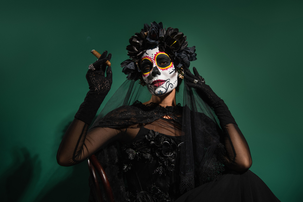 Kobieta z przerażającym Santa Muerte kostium gospodarstwa cygaro i pozowanie na zielonym tle  - Zdjęcie, obraz