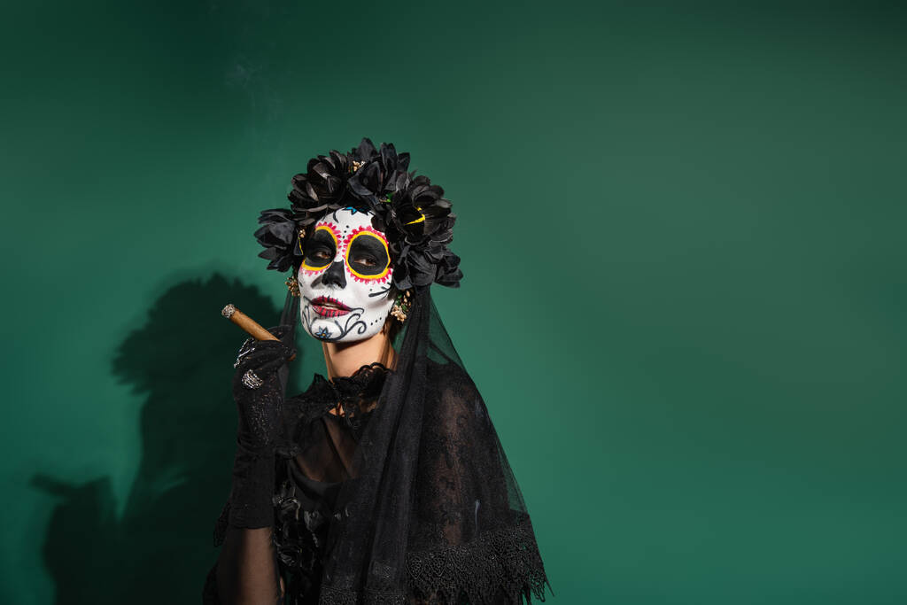 Mujer en el día de la muerte traje de Halloween celebración de cigarros sobre fondo verde  - Foto, imagen