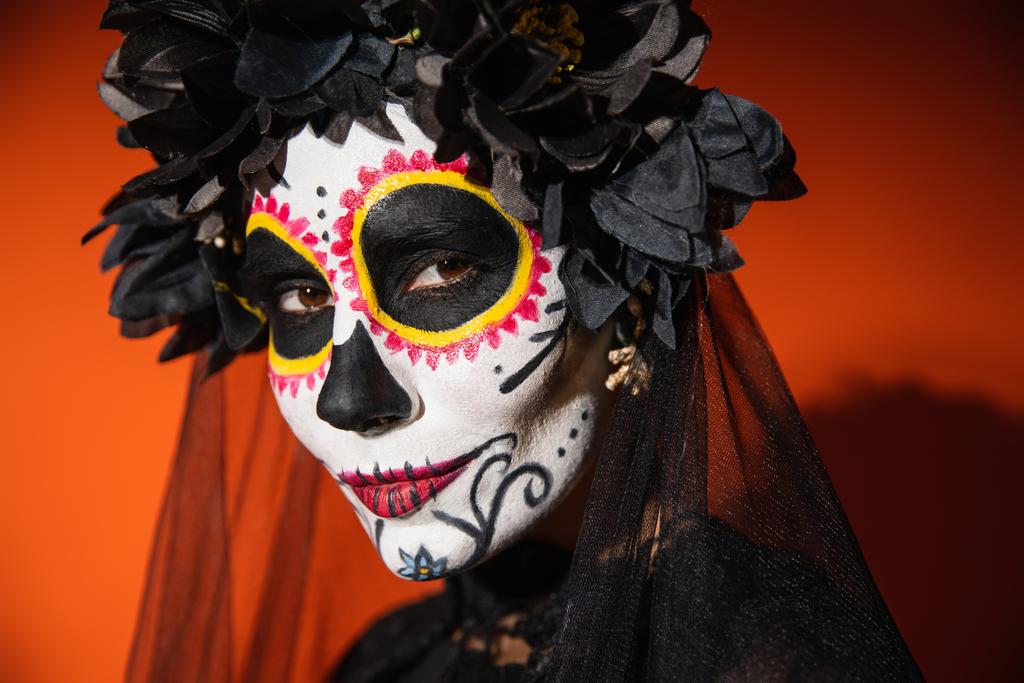 portrait of woman in catrina makeup and black wreath on orange background with dark shadow - Photo, Image