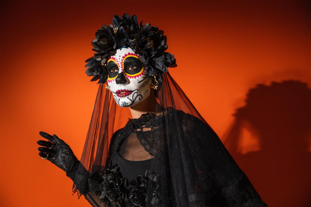 死んだ化粧のメキシコの日の女性と黒の不気味な衣装暗い影とオレンジの背景を離れて見て - 写真・画像