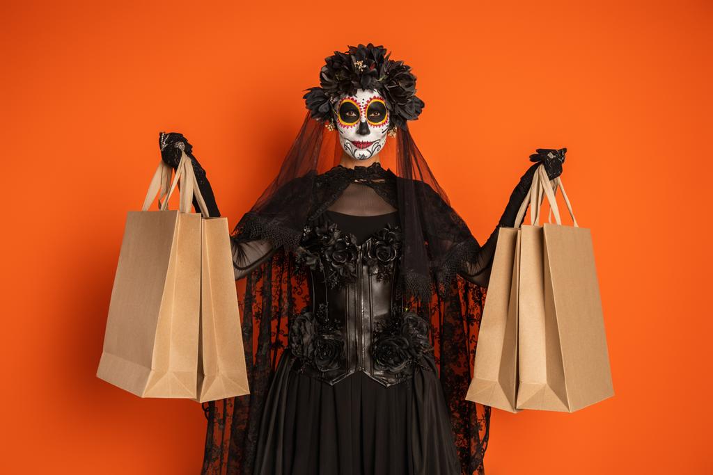 Frau in Catrina-Make-up und mexikanischem Totenkostüm mit Einkaufstüten in Orange - Foto, Bild