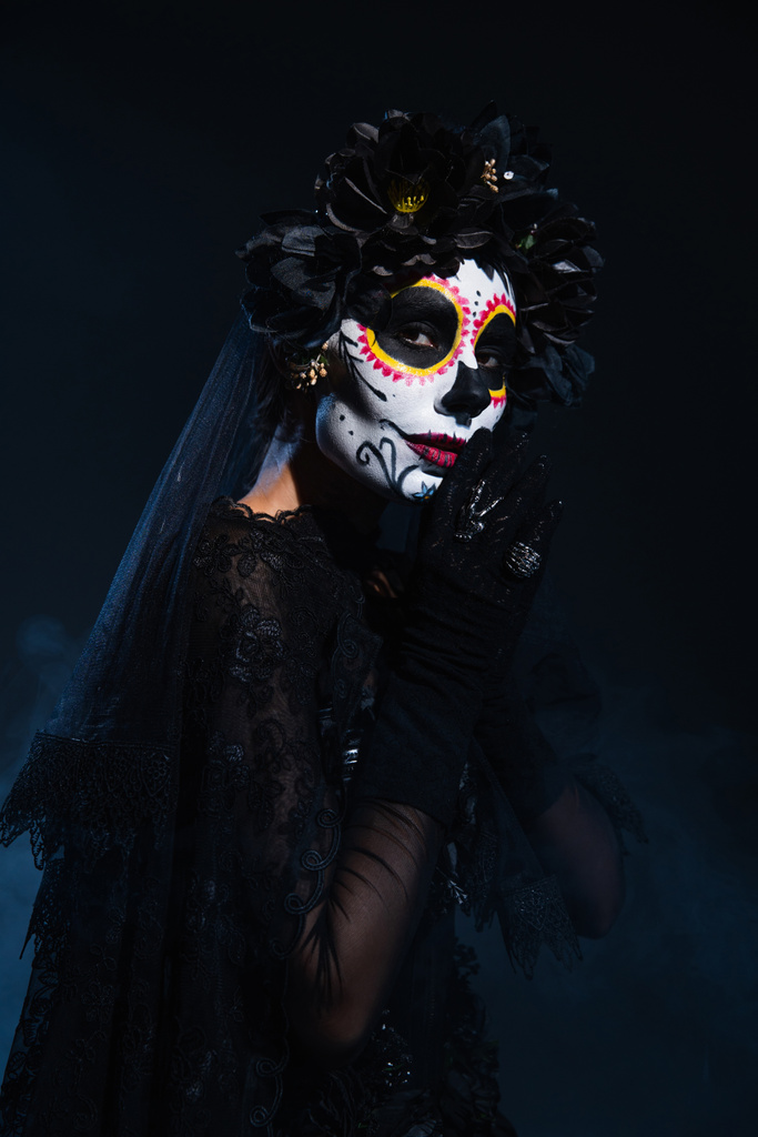 жінка в традиційному мексиканському дні мертвого макіяжу і костюмів стоїть з молитовними руками на темно-синьому фоні
 - Фото, зображення