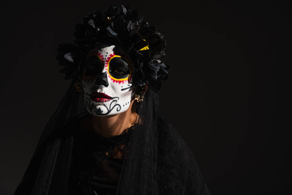 woman in halloween costume and sugar skull makeup looking at camera isolated on black - Photo, Image
