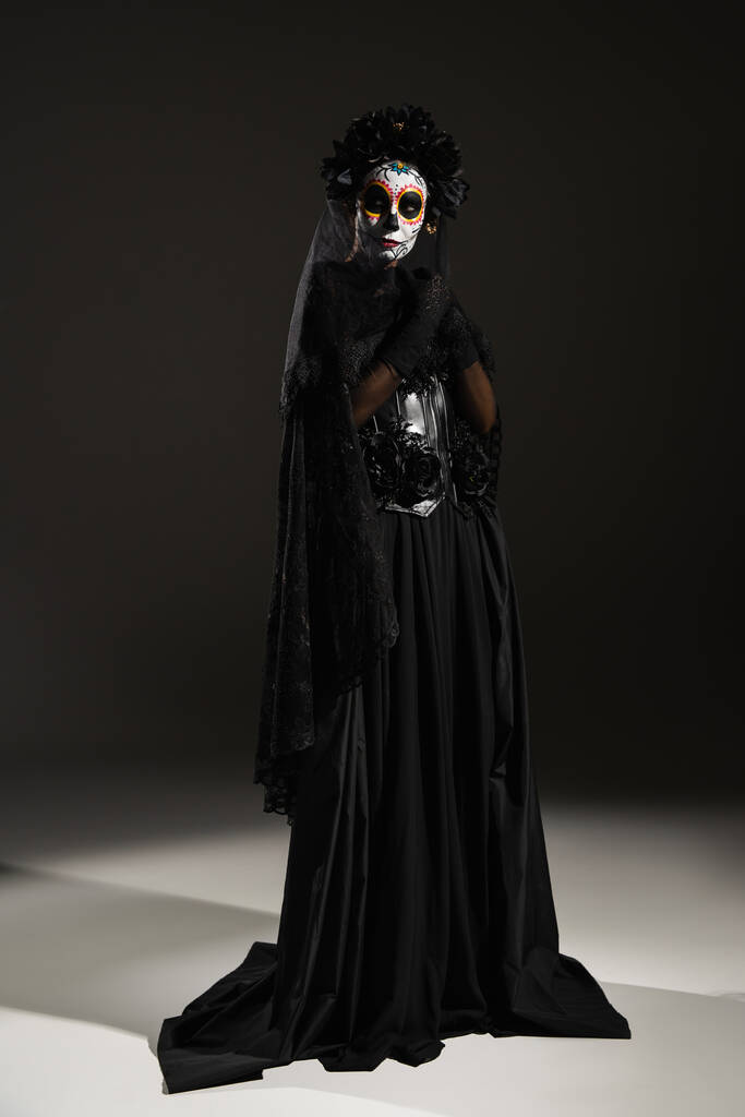 Полная длина женщины в жутком костюме и мексиканский день мертвого грима стоя на черном фоне - Фото, изображение