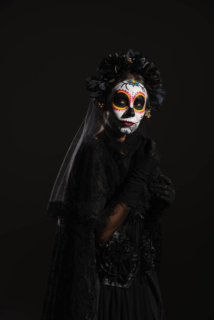 жінка в цукровому черепі макіяж і темний костюм Хеллоуїна з вуаллю дивиться ізольовано на чорному
 - Фото, зображення