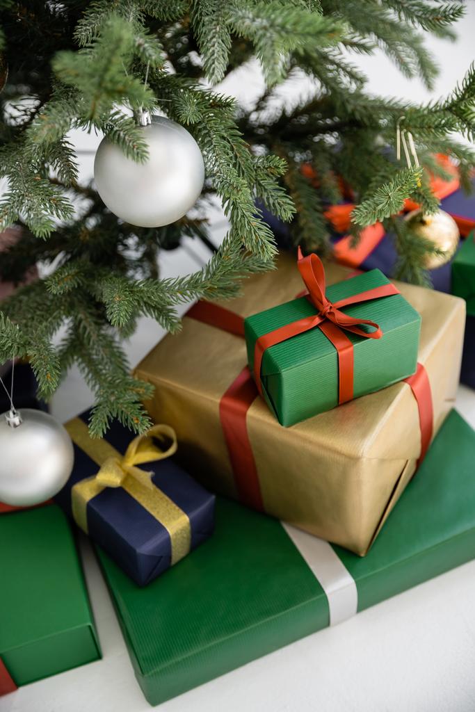 высокий угол обзора красочных подарочных коробок с лентами и бантами рядом с украшенной елкой  - Фото, изображение