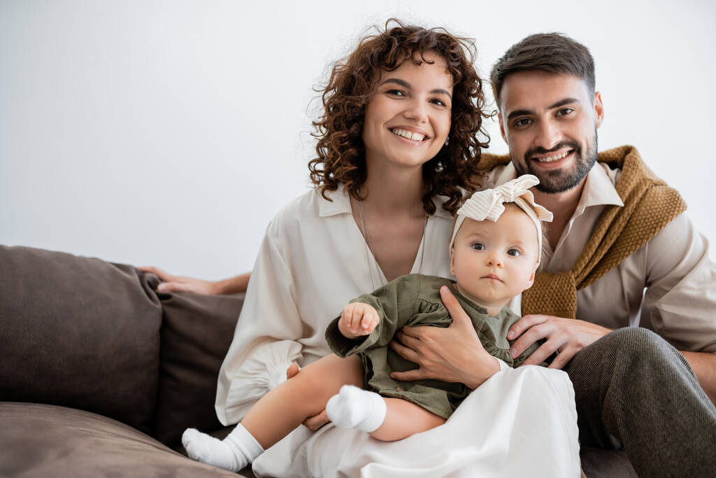 veselí rodiče drží holčičku v čelence a usmívá se v obývacím pokoji - Fotografie, Obrázek