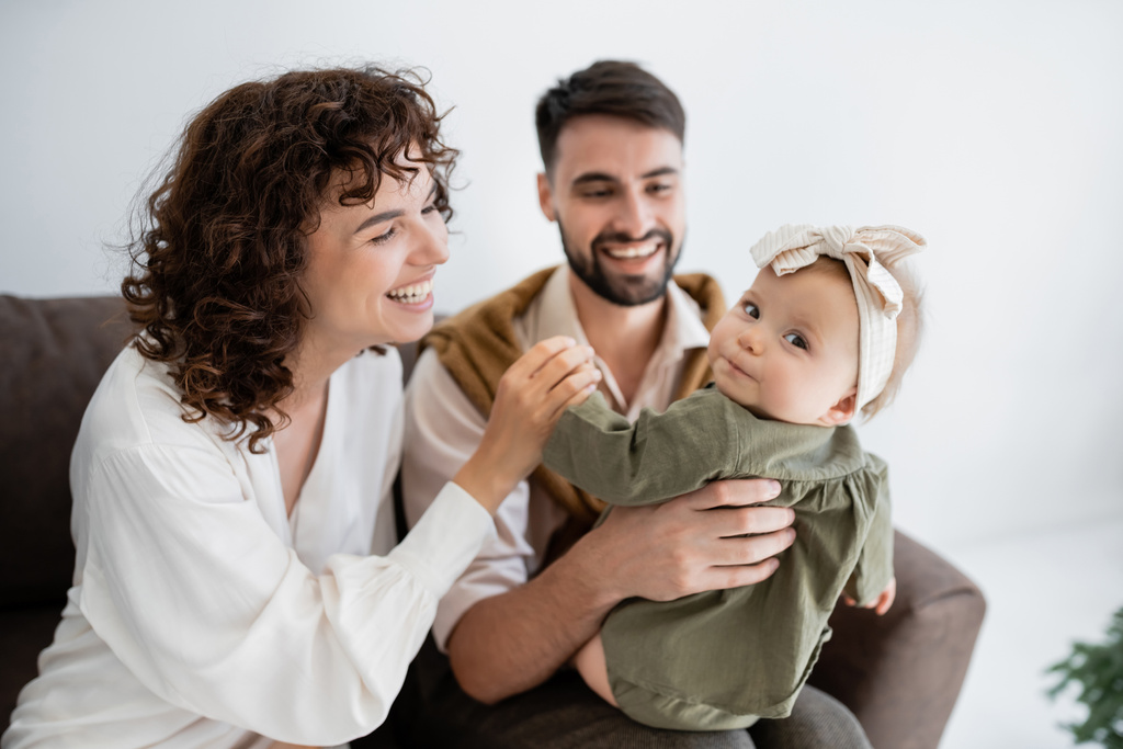 marido feliz e esposa segurando bebê menina na cabeça e sorrindo na sala de estar - Foto, Imagem