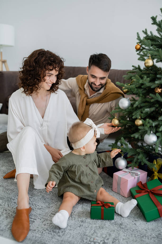 šťastná rodina s kojeneckou holčičku sedí v blízkosti vánočního stromečku s dárky  - Fotografie, Obrázek