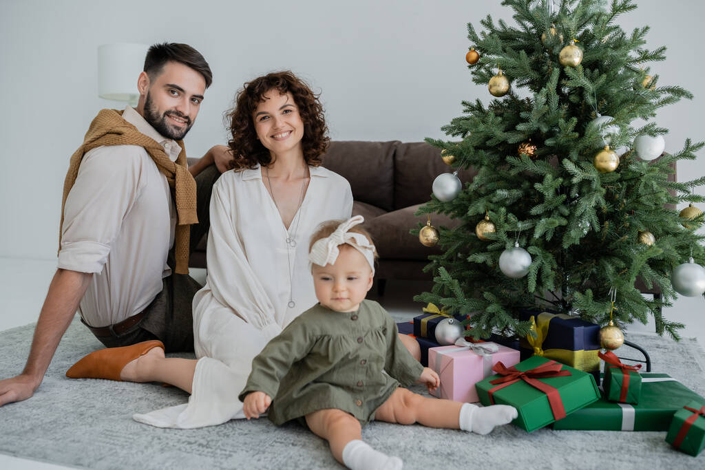 šťastní rodiče s kojeneckou dívkou sedí v blízkosti vánoční strom s dárky  - Fotografie, Obrázek