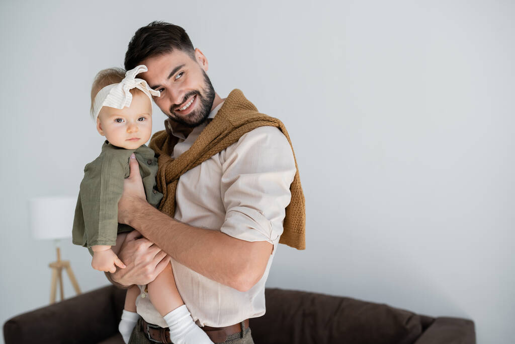 alegre barbudo hombre sosteniendo en brazos bebé niña en vestido y diadema  - Foto, Imagen