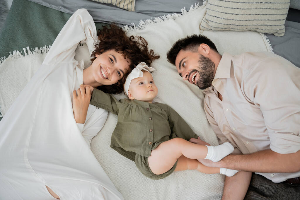vista superior de los padres positivos con niña acostada en la cama en casa  - Foto, Imagen