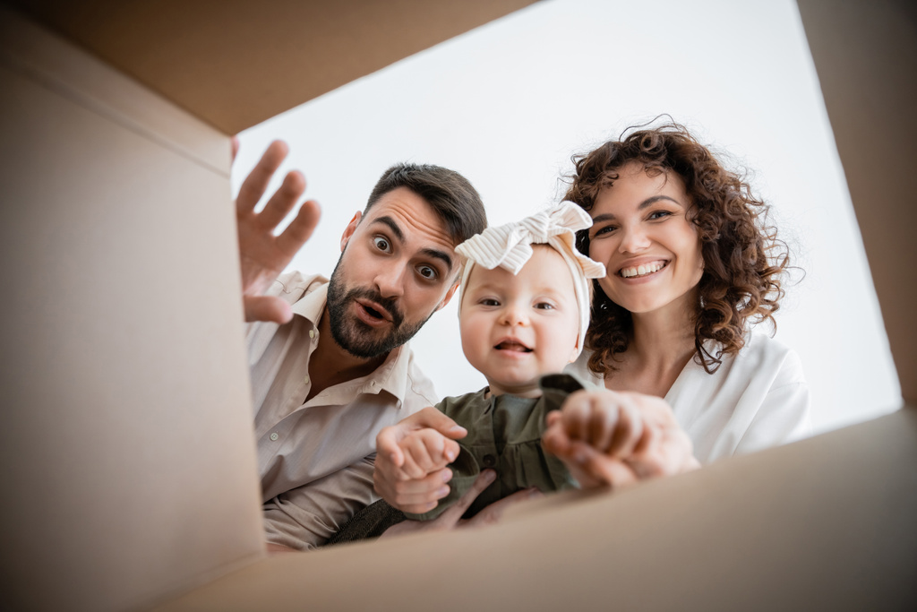 dolny widok radosnych rodziców i cute baby girl patrząc wewnątrz pudełka kartonowego - Zdjęcie, obraz