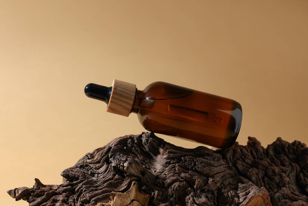 Láhev esenciálního oleje na stromové kůře proti tmavě béžové pozadí - Fotografie, Obrázek