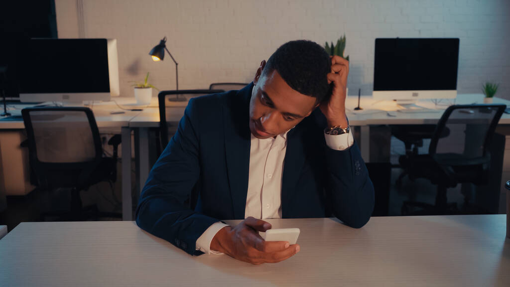 アフリカ系アメリカ人のマネージャーは、夜にオフィスで携帯電話を使用して正式な摩耗で  - 写真・画像