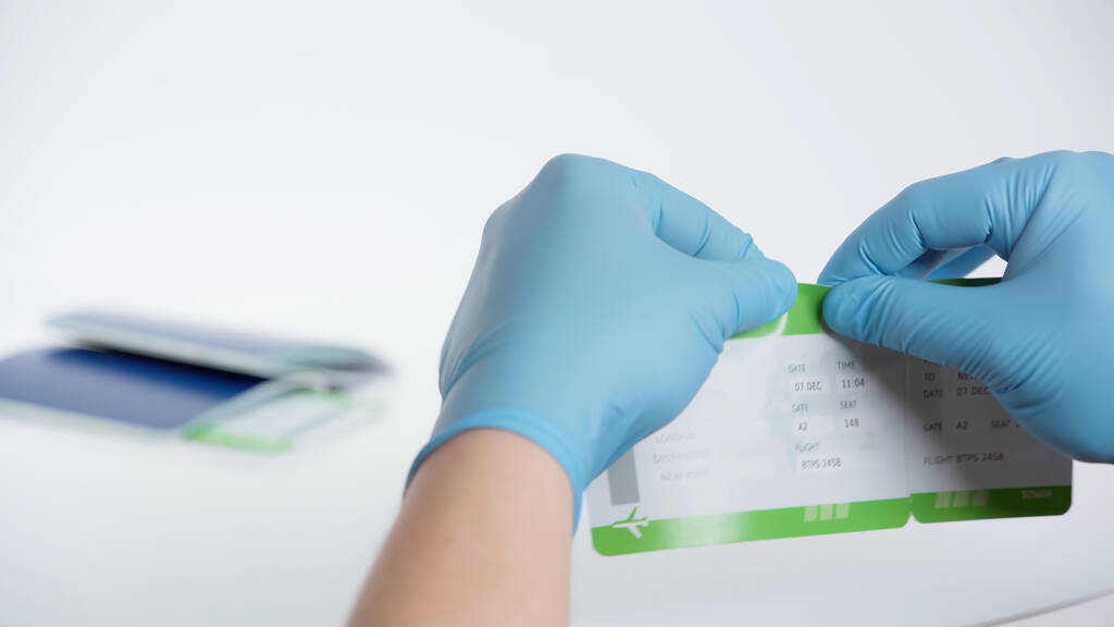 cropped view of man in latex gloves tearing boarding pass near blurred passport on white background - Photo, Image