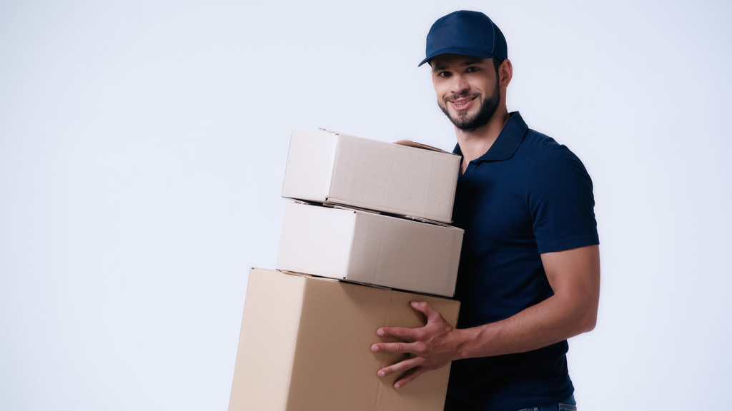 усміхнений чоловік доставки, що носить картонні коробки ізольовані на білому
 - Фото, зображення