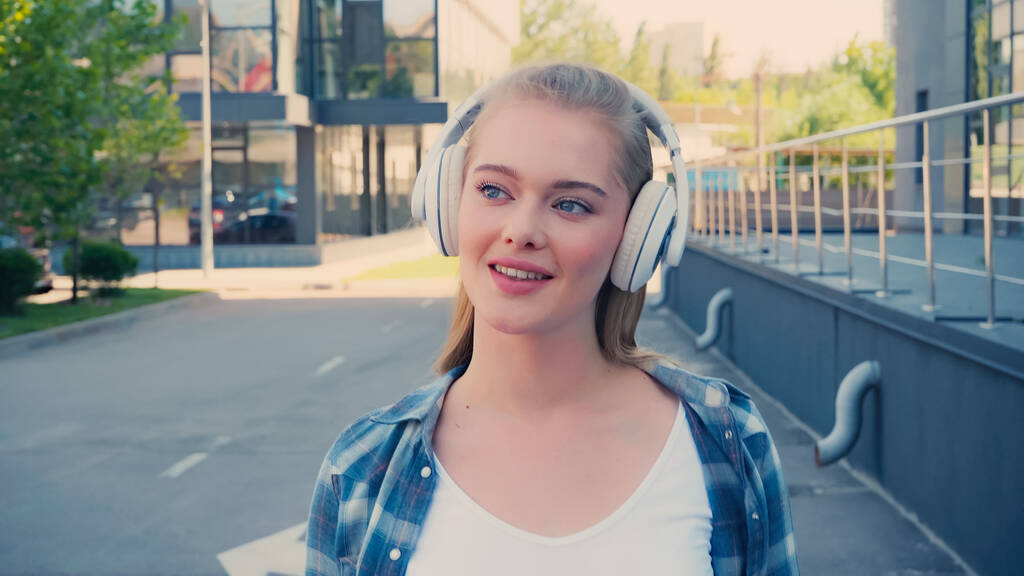 笑顔の女性は、都市部の通りにワイヤレスヘッドフォンで音楽を聞いて  - 写真・画像