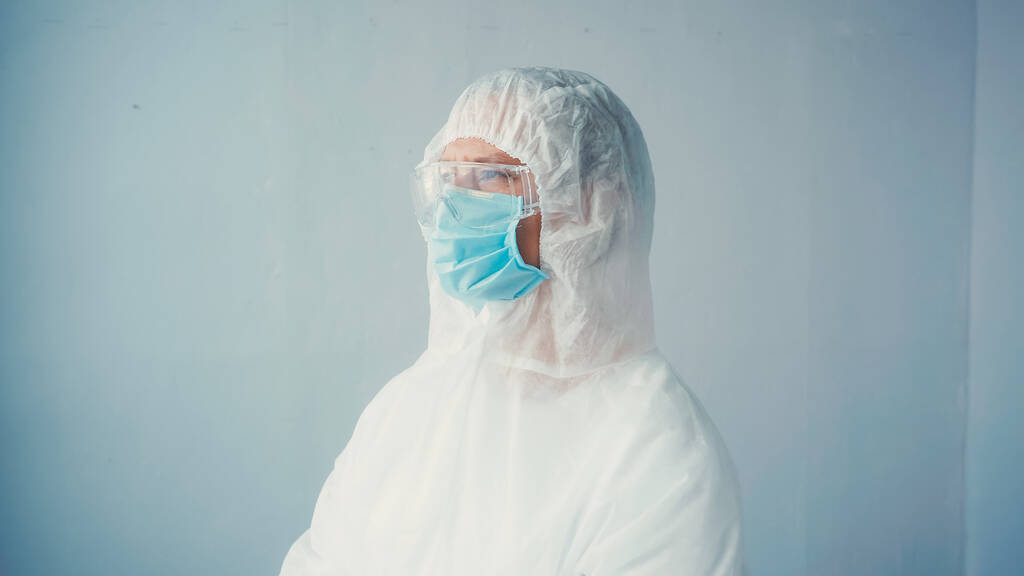 врач в защитном костюме и очках с медицинской маской на сером фоне - Фото, изображение