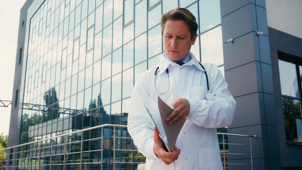 médecin en manteau blanc regardant le dossier avec des documents à l'extérieur - Photo, image