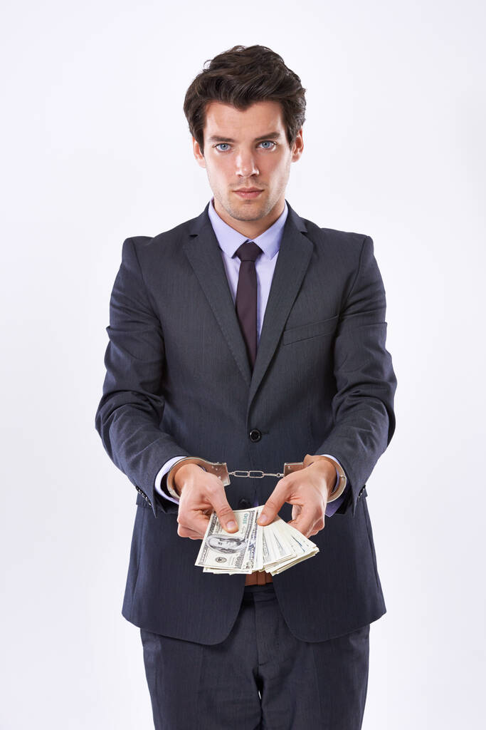 Can money buy my freedom. Studio shot of a handsome young businessman in handcuffs holding American Dollars - Photo, Image