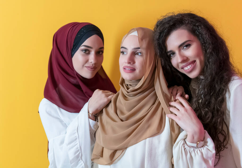 Групповые портреты красивых мусульманских женщин, две из которых в модном платье с хиджабом на желтом фоне. Высокое качество фото - Фото, изображение