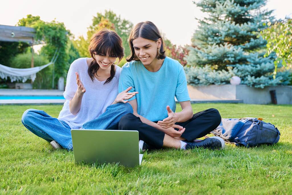 Dwóch nastoletnich przyjaciół uczniów siedzących na trawie z laptopem, na podwórku, chłopak i dziewczyna w wieku 18 lat uczą się razem. Przyjaźń, Młodzież, Technologia, Szkoła średnia, Szkoła wyższa, Koncepcja stylu życia - Zdjęcie, obraz