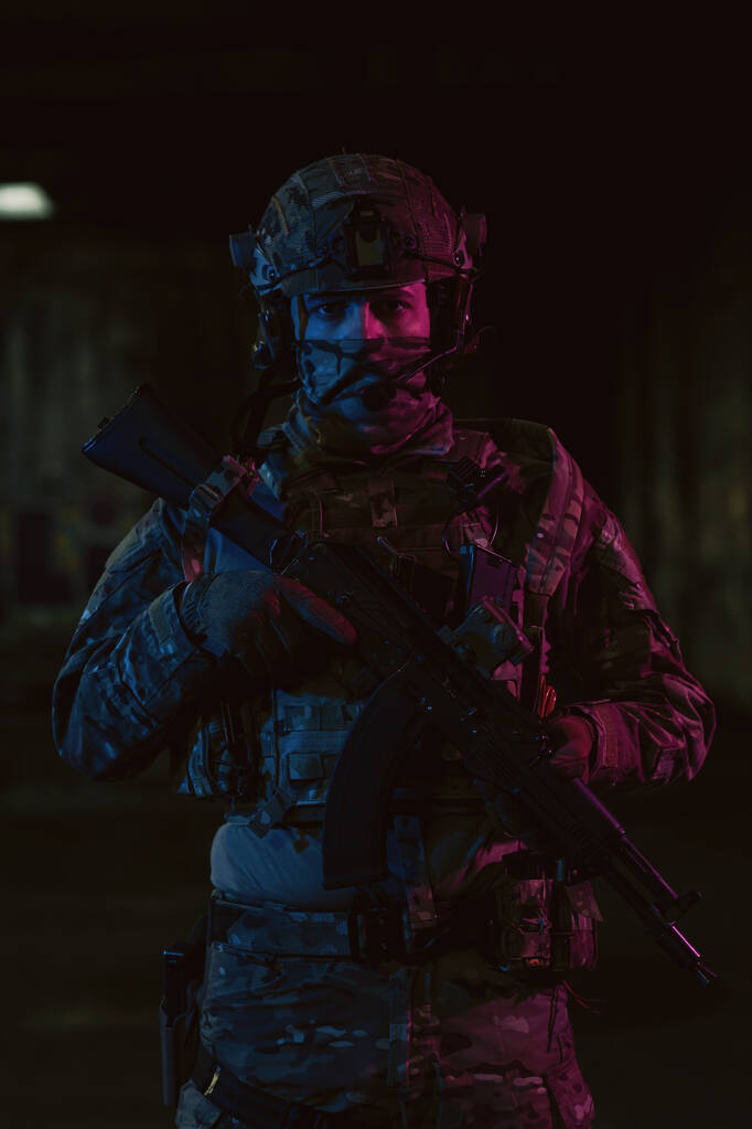 Soldado del ejército en uniformes de combate con un rifle de asalto y casco de combate misión nocturna fondo oscuro. Efecto de luz de gel azul y púrpura. Foto de alta calidad - Foto, Imagen
