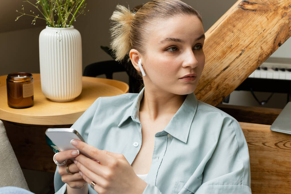 Mujer joven en auriculares con teléfono inteligente en la sala de estar  - Foto, imagen