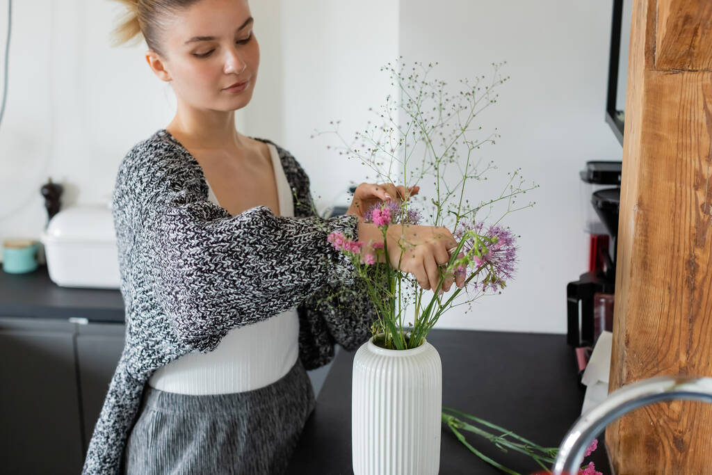 ニットカーディガンの女性は台所の花瓶に花を置く  - 写真・画像