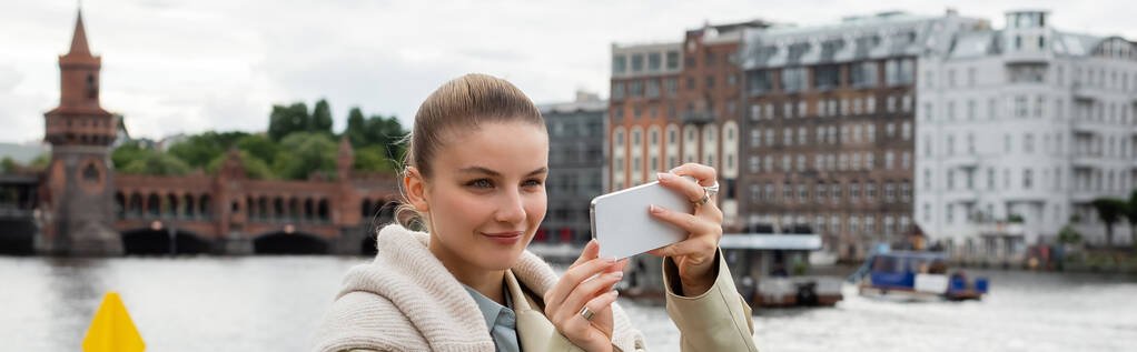 счастливая молодая женщина, фотографирующаяся на смартфон на улице в Берлине, баннер  - Фото, изображение