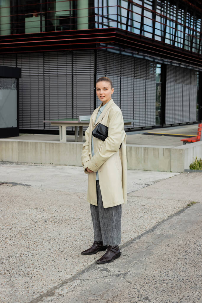 Mulher elegante em casaco de trincheira olhando para a câmera na rua urbana em Berlim  - Foto, Imagem