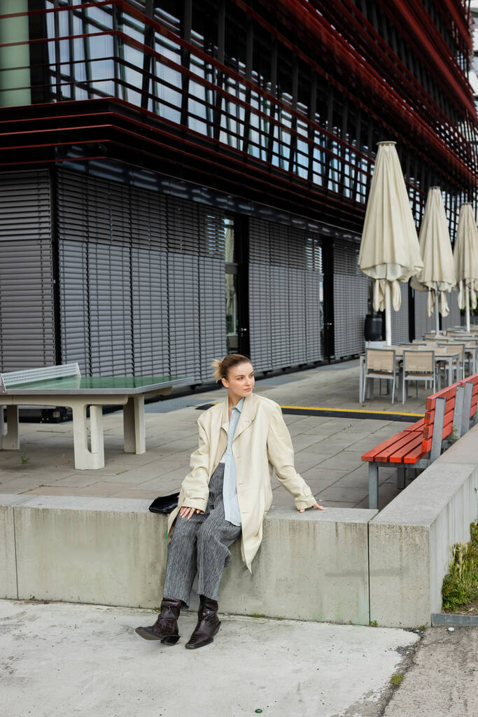 Stylowy podróżnik w płaszczu z widokiem na budynek na ulicy w Niemczech  - Zdjęcie, obraz