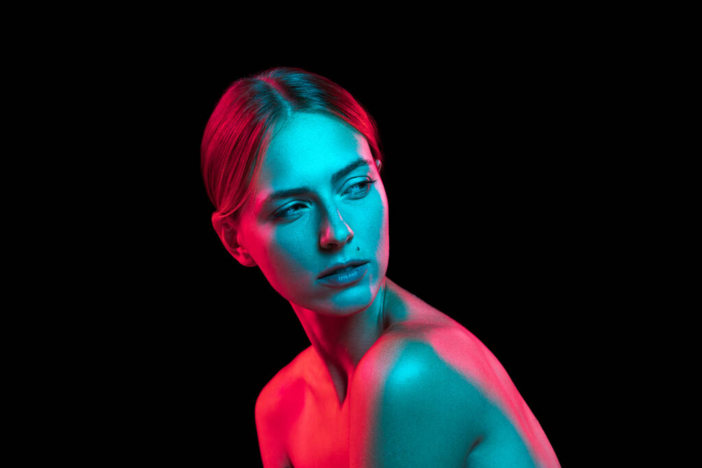 Nahaufnahme Porträt einer jungen hübschen Frau mit nackten Schultern in rotem Neonlicht auf dunklem Hintergrund. Kunst, Kreativität, Mode, Stil. Seriöses und durchdachtes Modell - Foto, Bild
